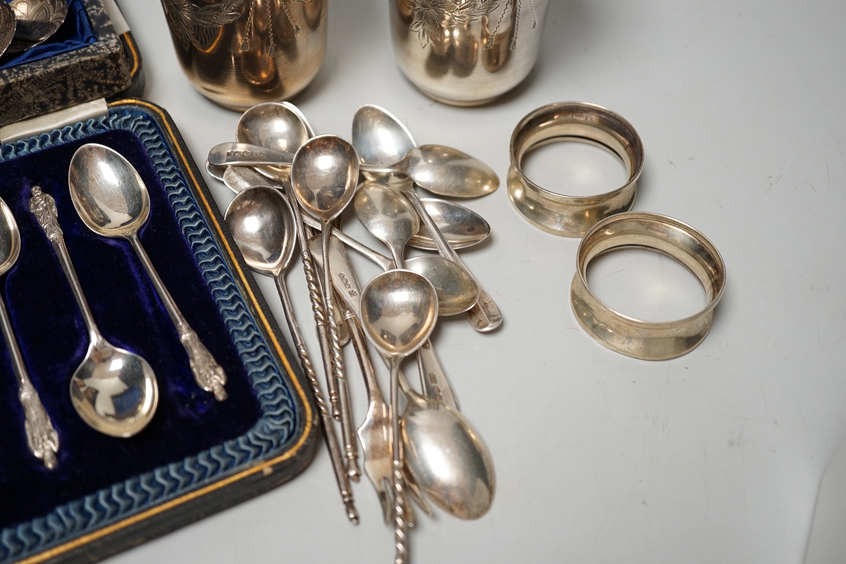 A pair of engraved white metal tumblers, stamped 'K980', four Russian 84 zolotnik spoon, a cased set of silver silver teaspoons with tongs, two silver napkin rings and other minor silver and white metal flatware.